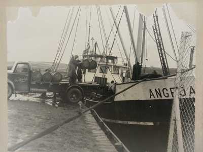 This photograph is dated to March 1953. The caption reads 'Unloading of Glucose at Letterkenny Port'. Glucose was shipped form around the world to make sweets at the Oatfield Factory in Letterkenny. The location is likely the Thorn Pier just outside Letterkenny town on the shores of the River Swilly to the east. (DCM.2025.78)